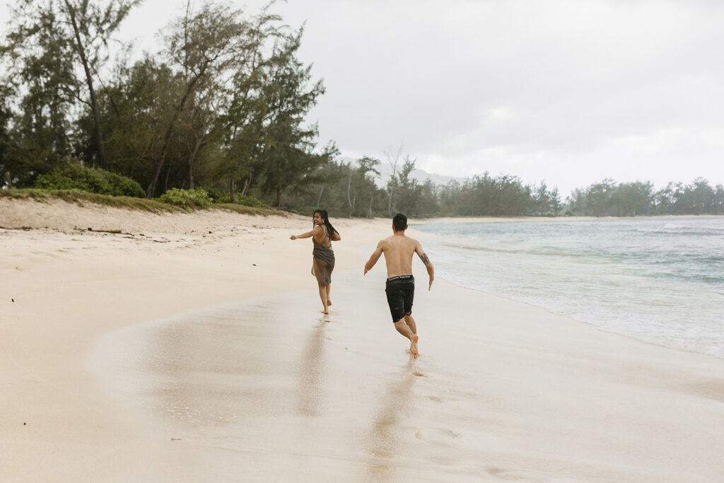 couple playing and running on a beach in oahu
