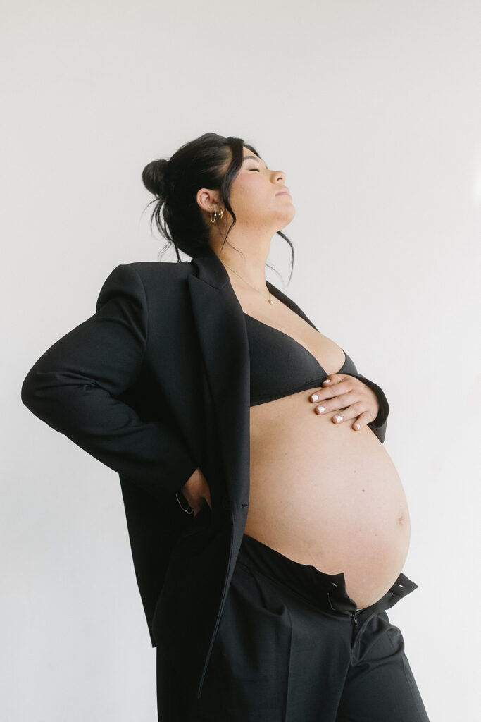Pregnant woman holding baby bump in a clean, timeless studio setting

