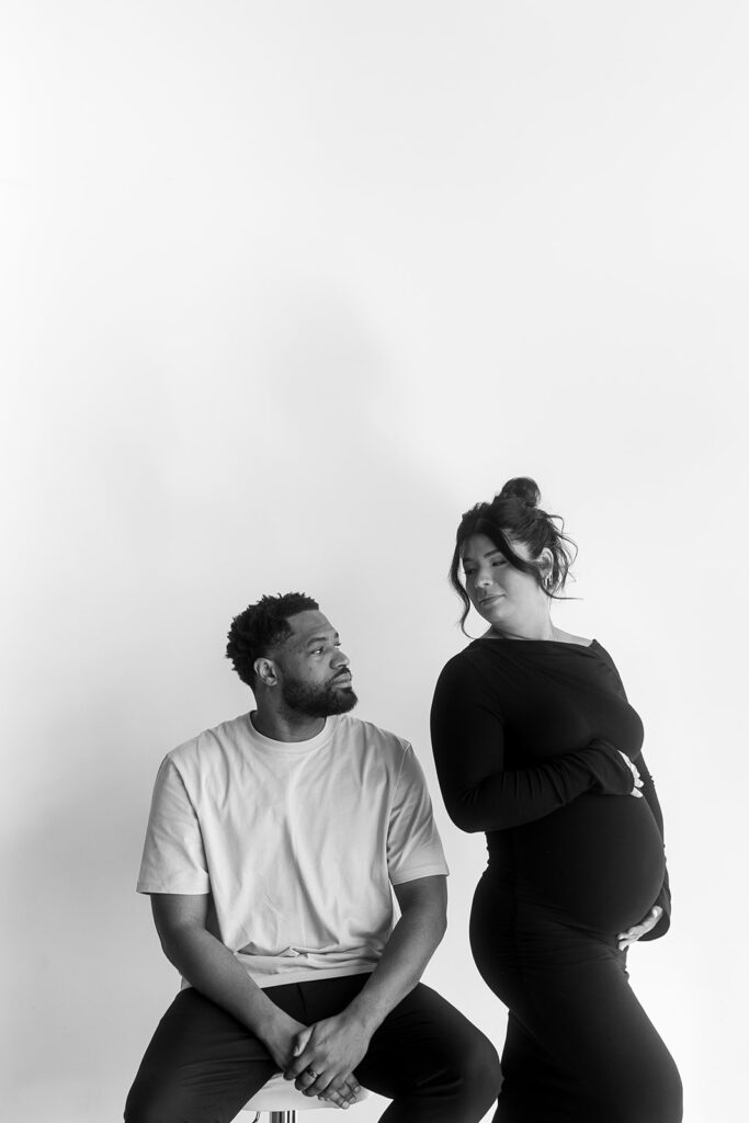 Pregnant woman holding baby bump in a clean, timeless studio setting
