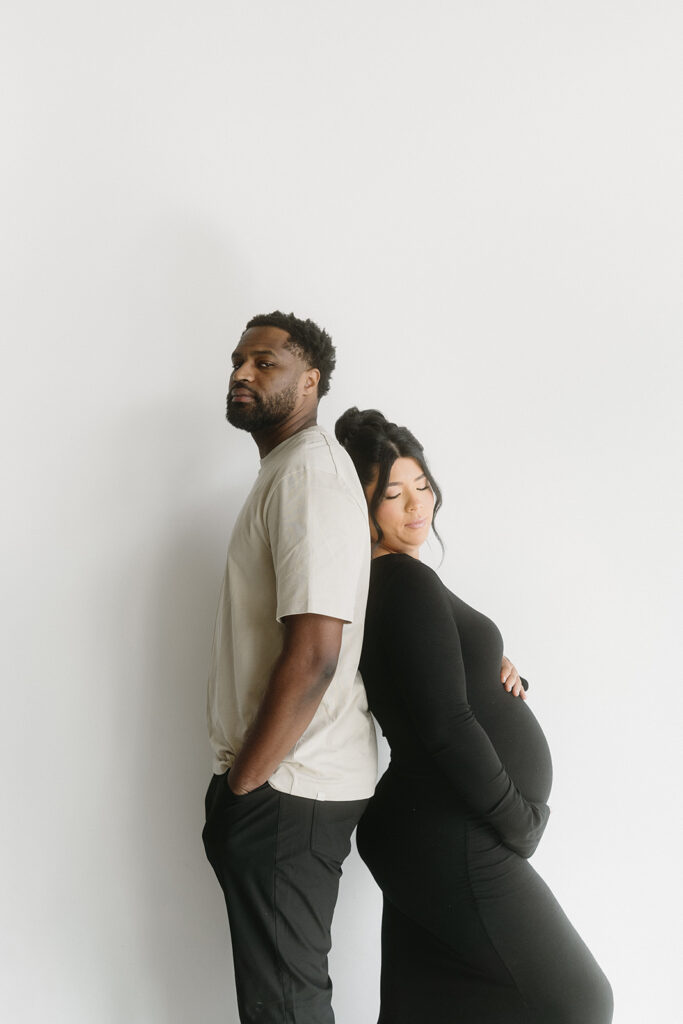 Pregnant woman holding baby bump in a clean, timeless studio setting
