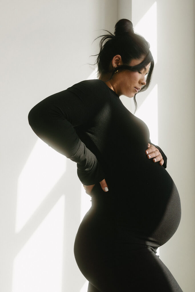 Pregnant woman holding baby bump in a clean, timeless studio setting
