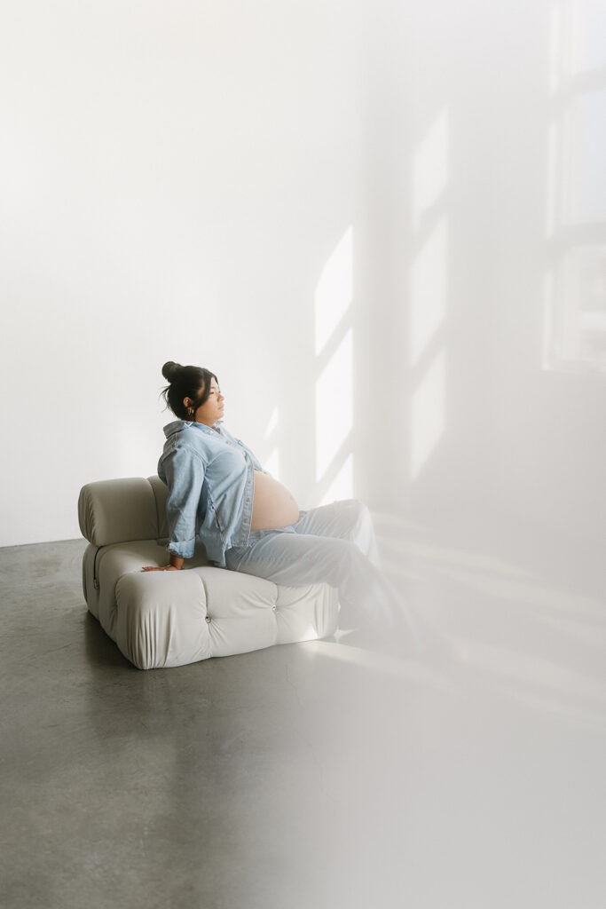 Pregnant woman holding baby bump in a clean, timeless studio setting
