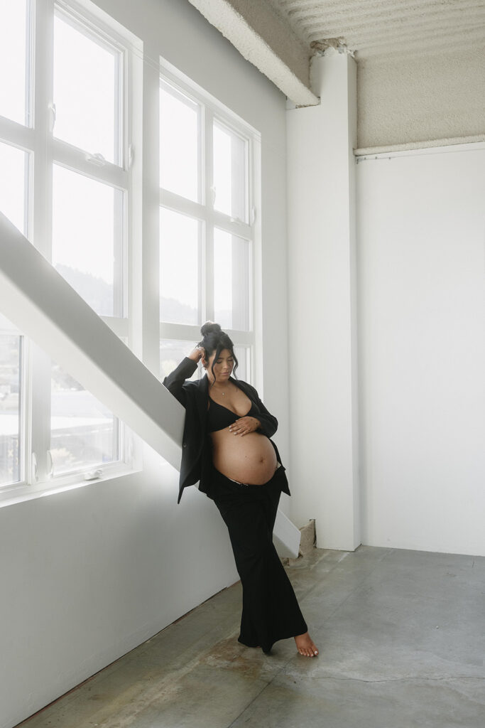 Pregnant woman holding baby bump in a clean, timeless studio setting
