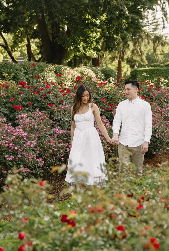 A couple walking through a blooming rose garden during their engagement session | Peninsula Rose Garden
