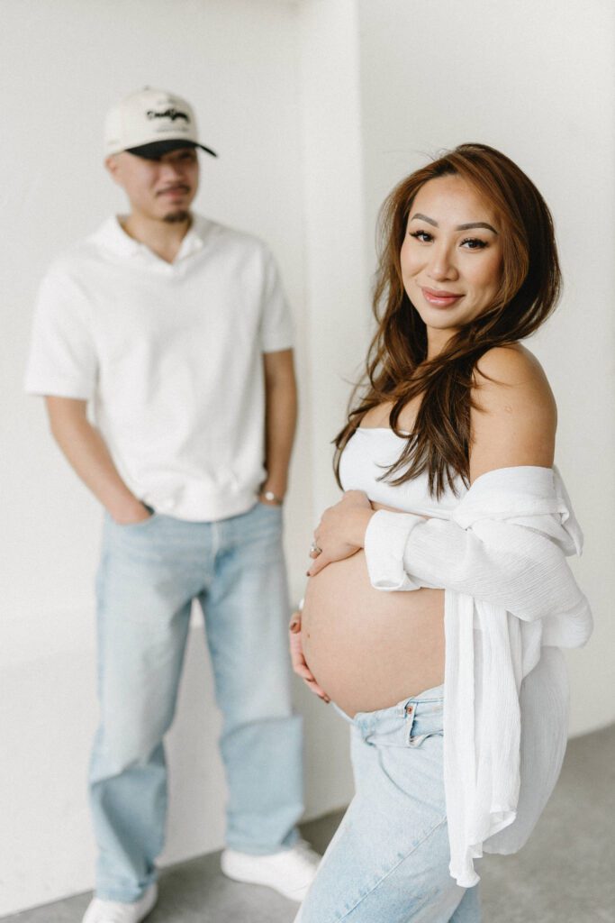 Pregnant woman standing in natural light holding her belly.
