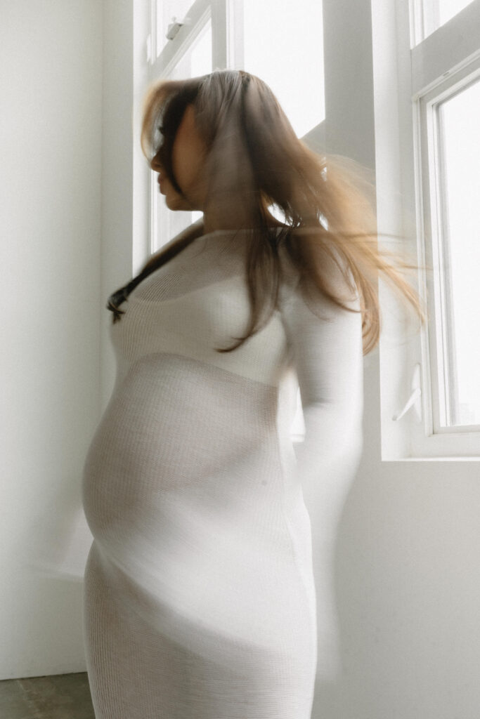 Pregnant woman standing in natural light holding her belly.
