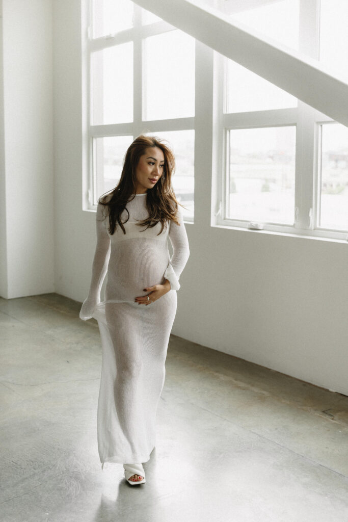 Pregnant woman standing in natural light holding her belly.
