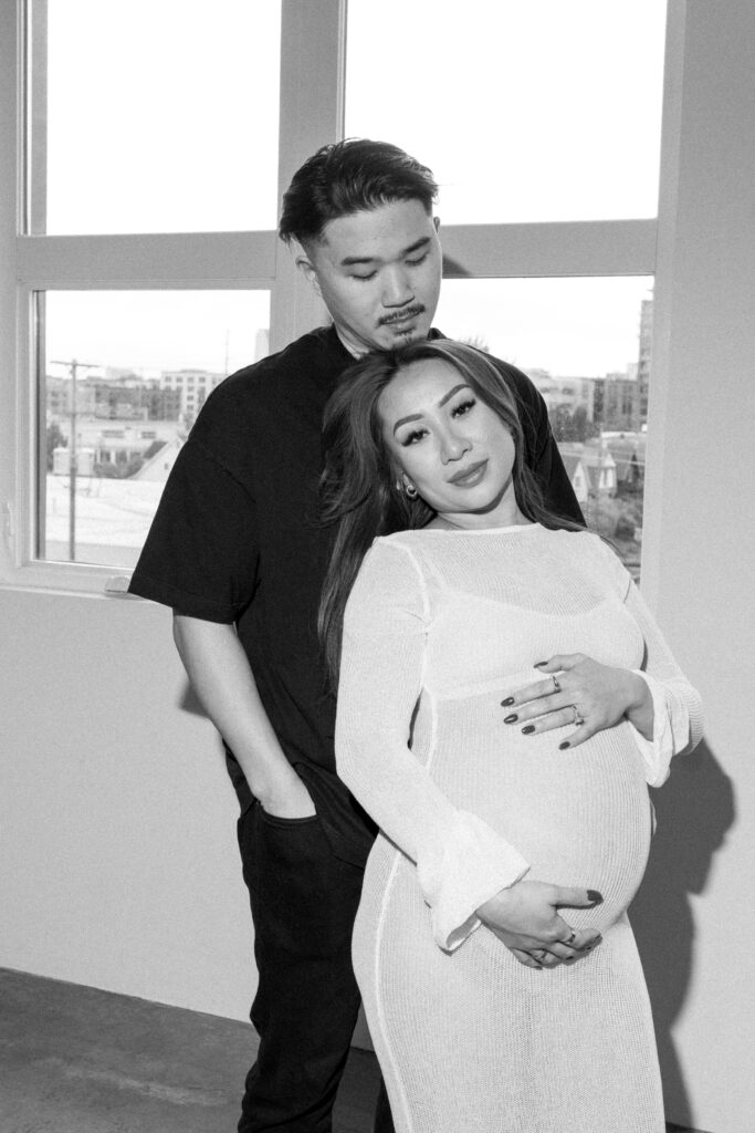 Expecting parents sharing a candid moment in a minimalist studio space.
