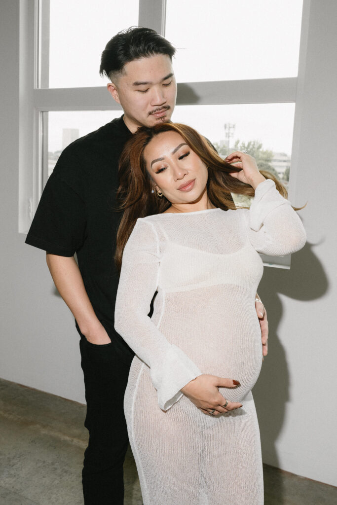 Expecting parents sharing a candid moment in a minimalist studio space.
