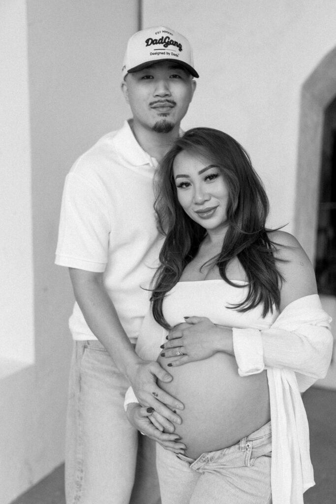 Pregnant woman standing in natural light holding her belly.
