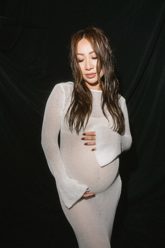 Expecting parents sharing a candid moment in a minimalist studio space.
