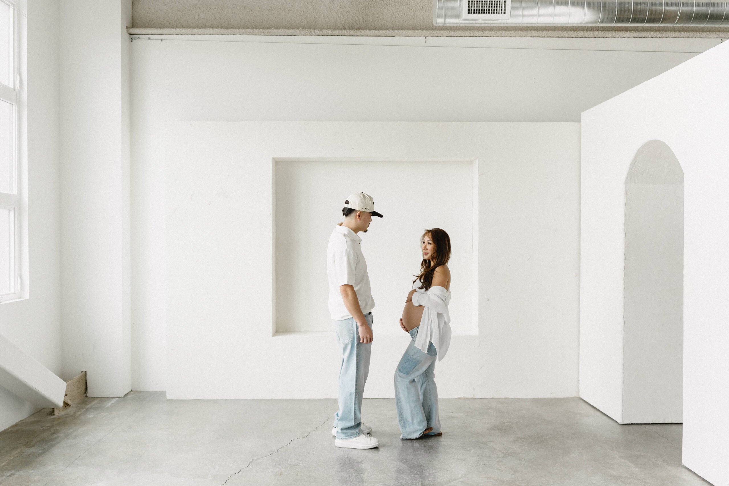 Couple posing during a modern maternity photoshoot in a bright studio.