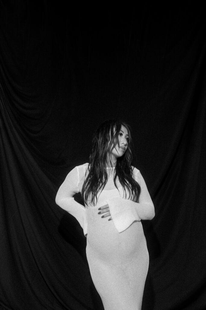 Pregnant woman standing in natural light holding her belly.
