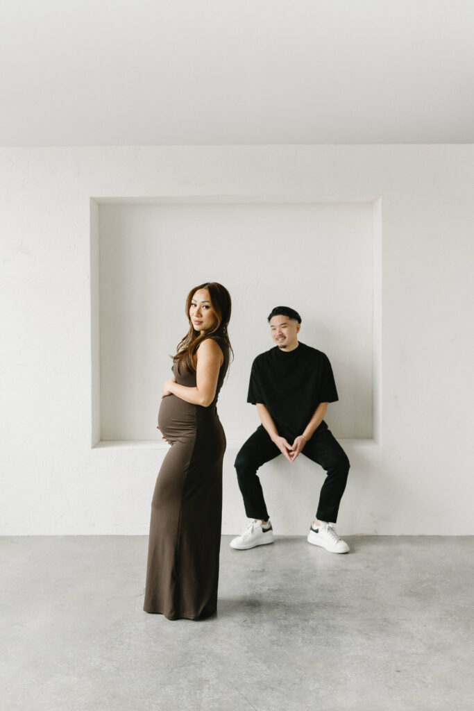 Couple posing during a modern maternity photoshoot in a bright studio.
