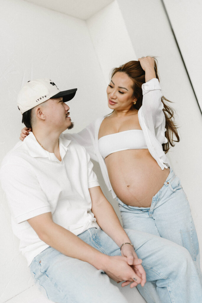 Pregnant woman standing in natural light holding her belly.
