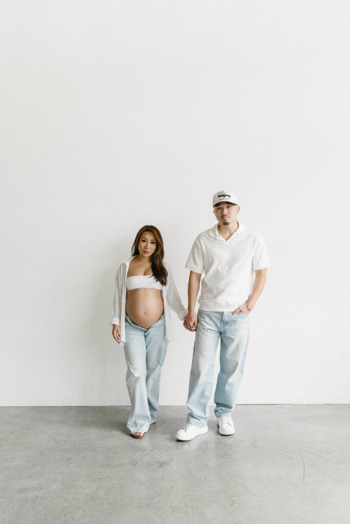 Pregnant woman standing in natural light holding her belly.
