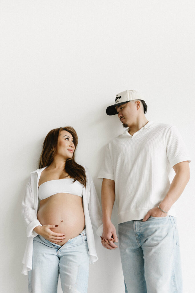 Expecting parents sharing a candid moment in a minimalist studio space.
