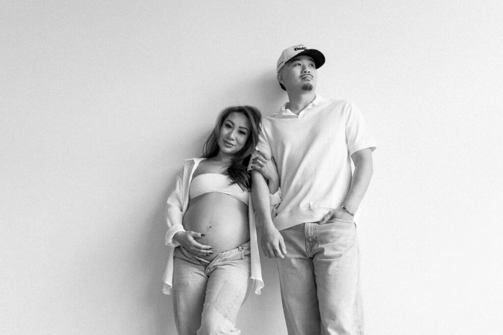 Expecting parents sharing a candid moment in a minimalist studio space.
