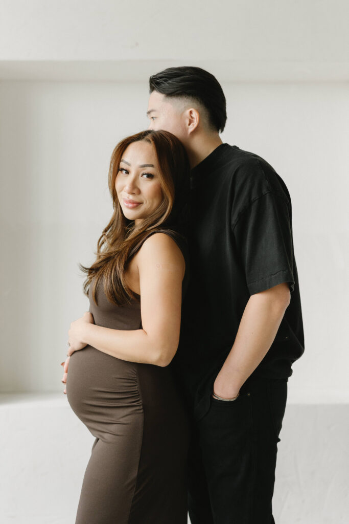 Couple posing during a modern maternity photoshoot in a bright studio.
