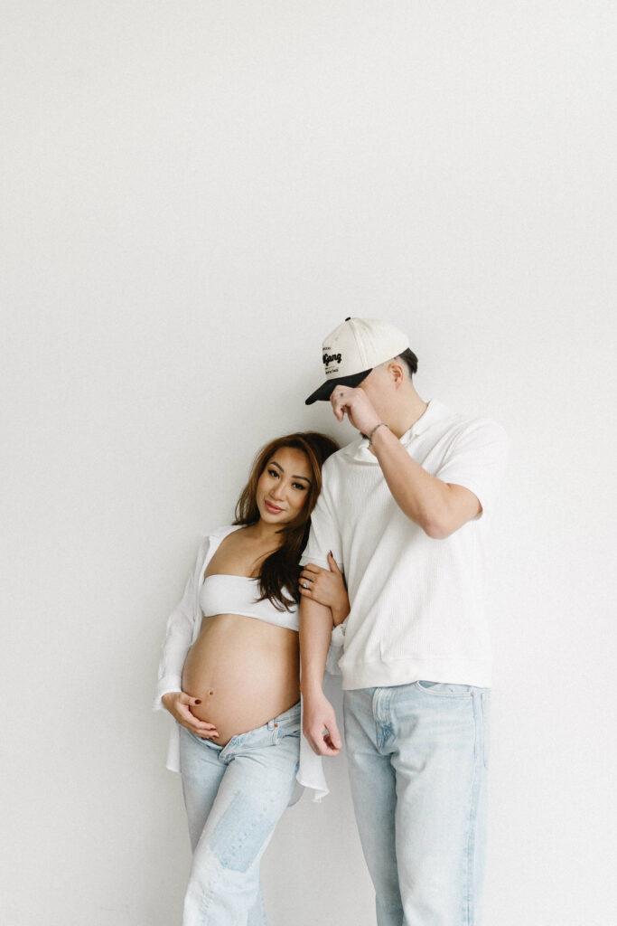 Expecting parents sharing a candid moment in a minimalist studio space.
