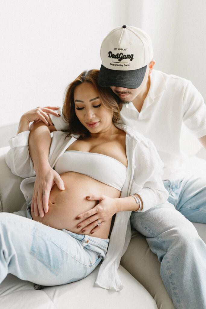 Couple posing during a modern maternity photoshoot in a bright studio.
