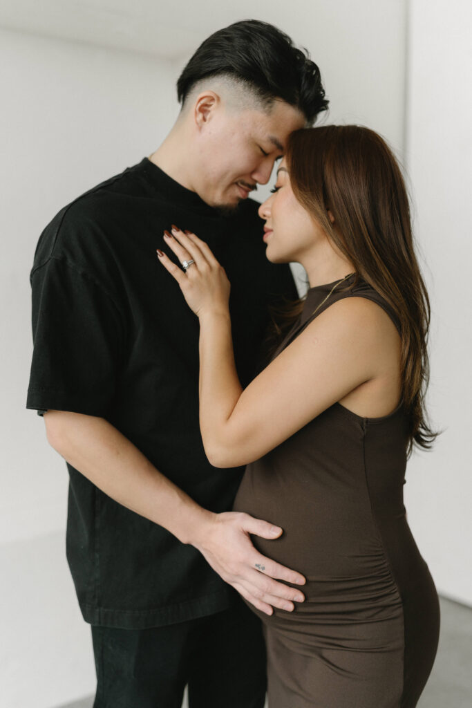 Couple posing during a modern maternity photoshoot in a bright studio.
