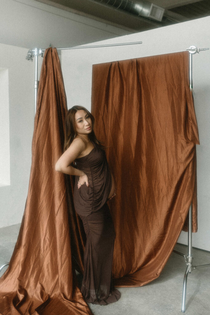 Creative maternity photoshoot with artistic draping and warm lighting.
