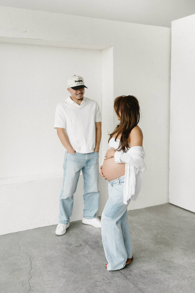 Pregnant woman standing in natural light holding her belly.
