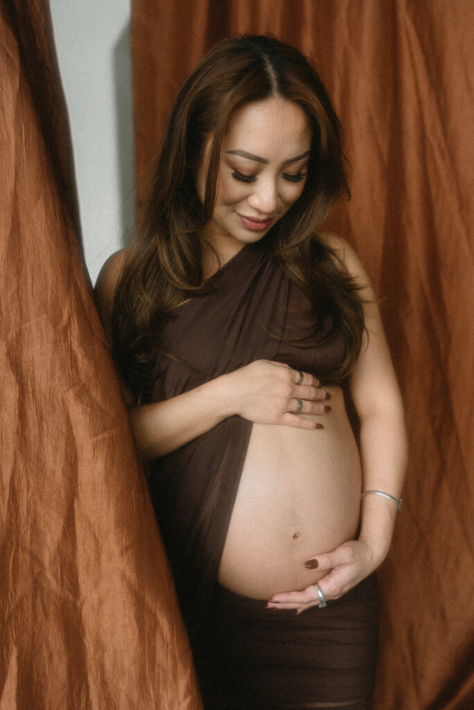 Pregnant woman standing in natural light holding her belly.
