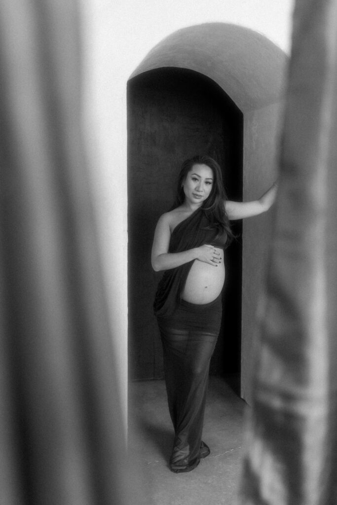 Pregnant woman standing in natural light holding her belly.
