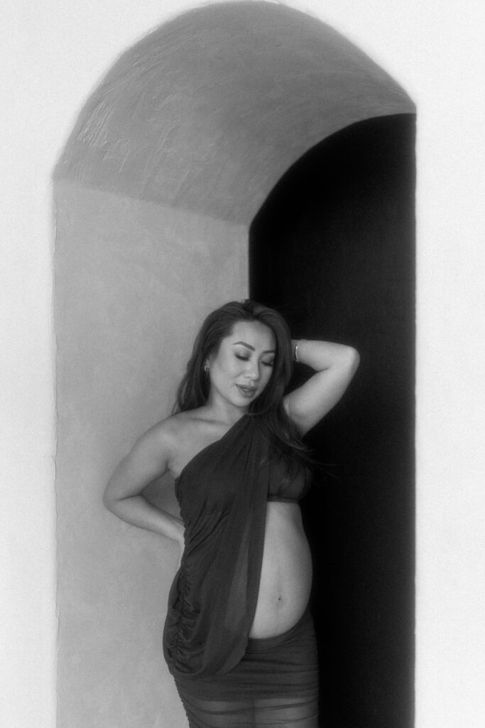 Pregnant woman standing in natural light holding her belly.
