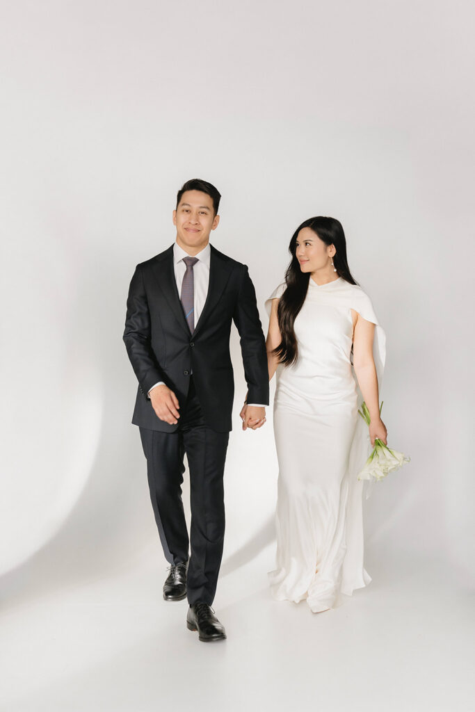 Elegant couple standing together in a minimalist studio with soft natural light and neutral tones.
