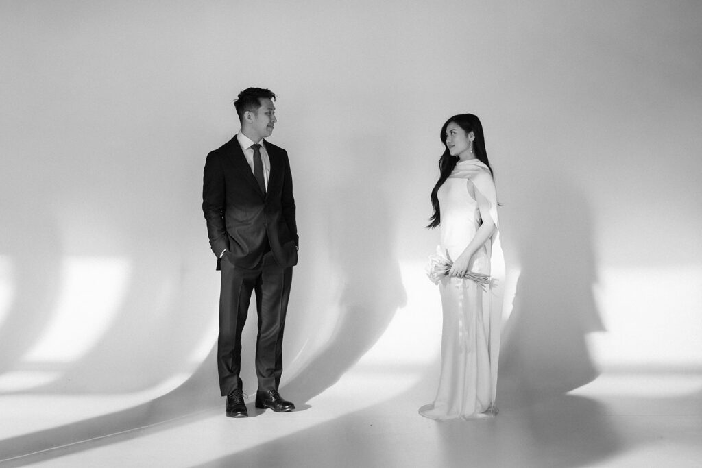 Elegant couple standing together in a minimalist studio with soft natural light and neutral tones.
