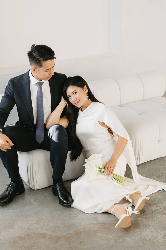 Elegant couple standing together in a minimalist studio with soft natural light and neutral tones.
