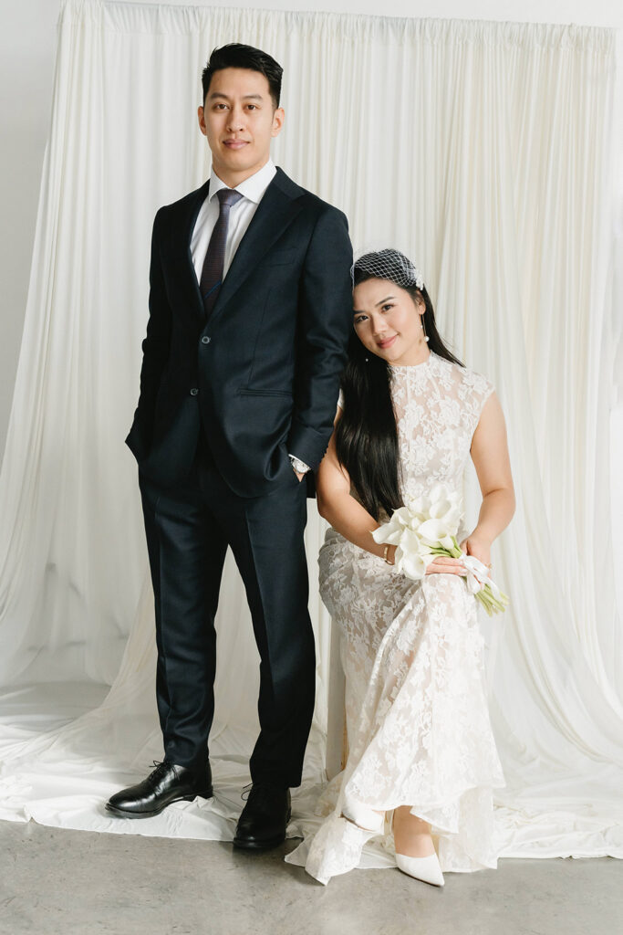 Elegant couple standing together in a minimalist studio with soft natural light and neutral tones.
