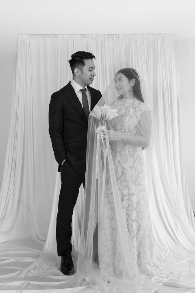 Elegant couple standing together in a minimalist studio with soft natural light and neutral tones.
