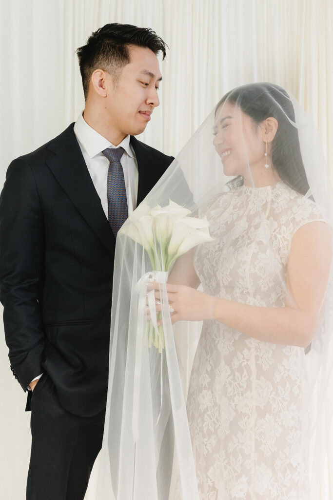 Bride holding a bouquet of white flowers while posing for timeless indoor wedding portraits.
