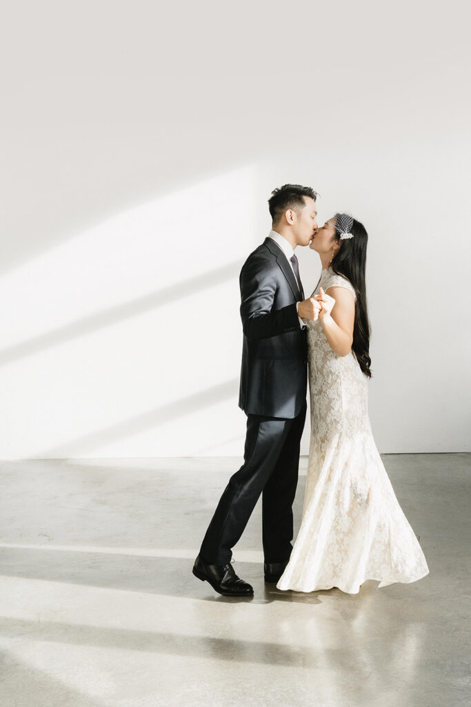 Elegant couple standing together in a minimalist studio with soft natural light and neutral tones.
