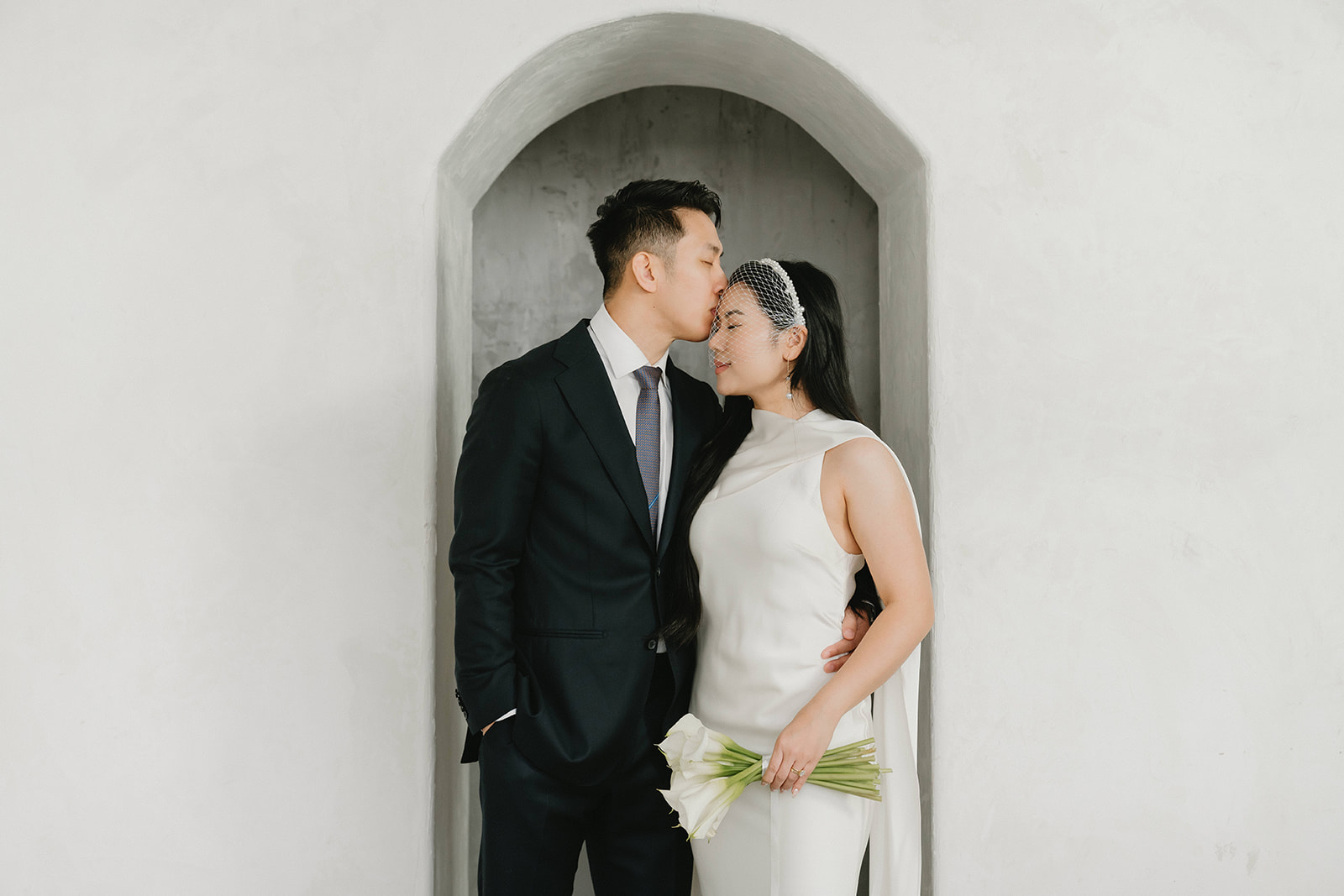 Bride and groom sharing a kiss during timeless and elegant pre-wedding portraits in studio in Portland at Cream Creative Space with soft natural light and minimal white backdrop.