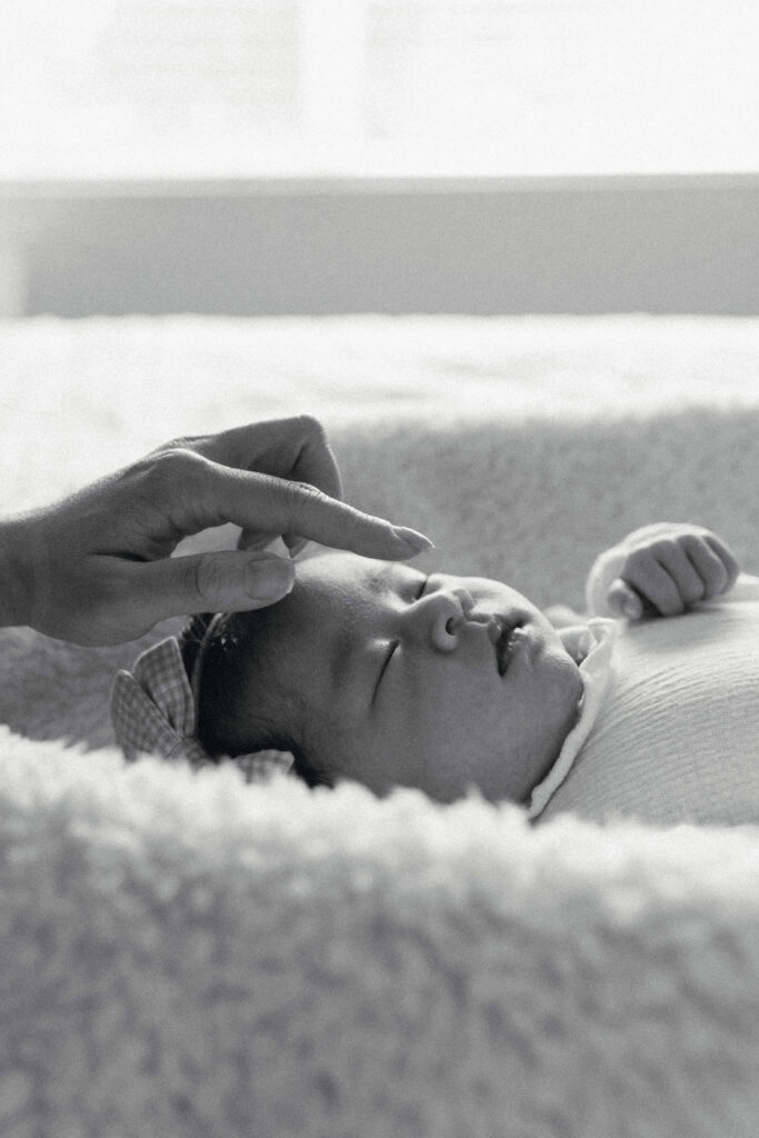 Mother gently holding her sleeping newborn during a calm in home newborn photoshoot by the window
