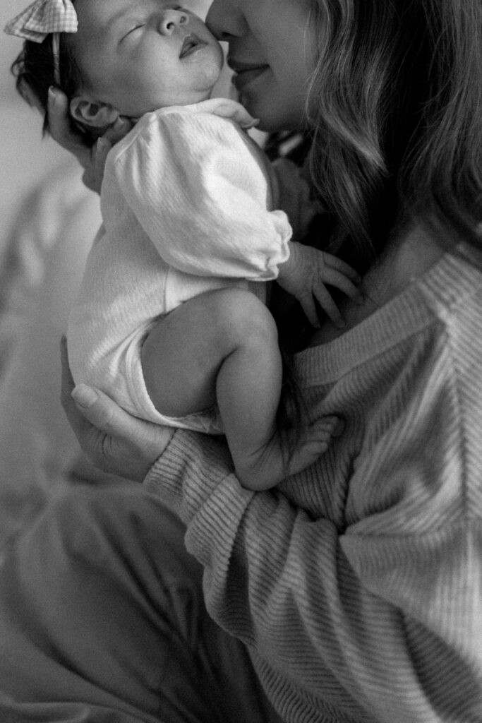 Mother gently holding her sleeping newborn during a calm in home newborn photoshoot by the window
