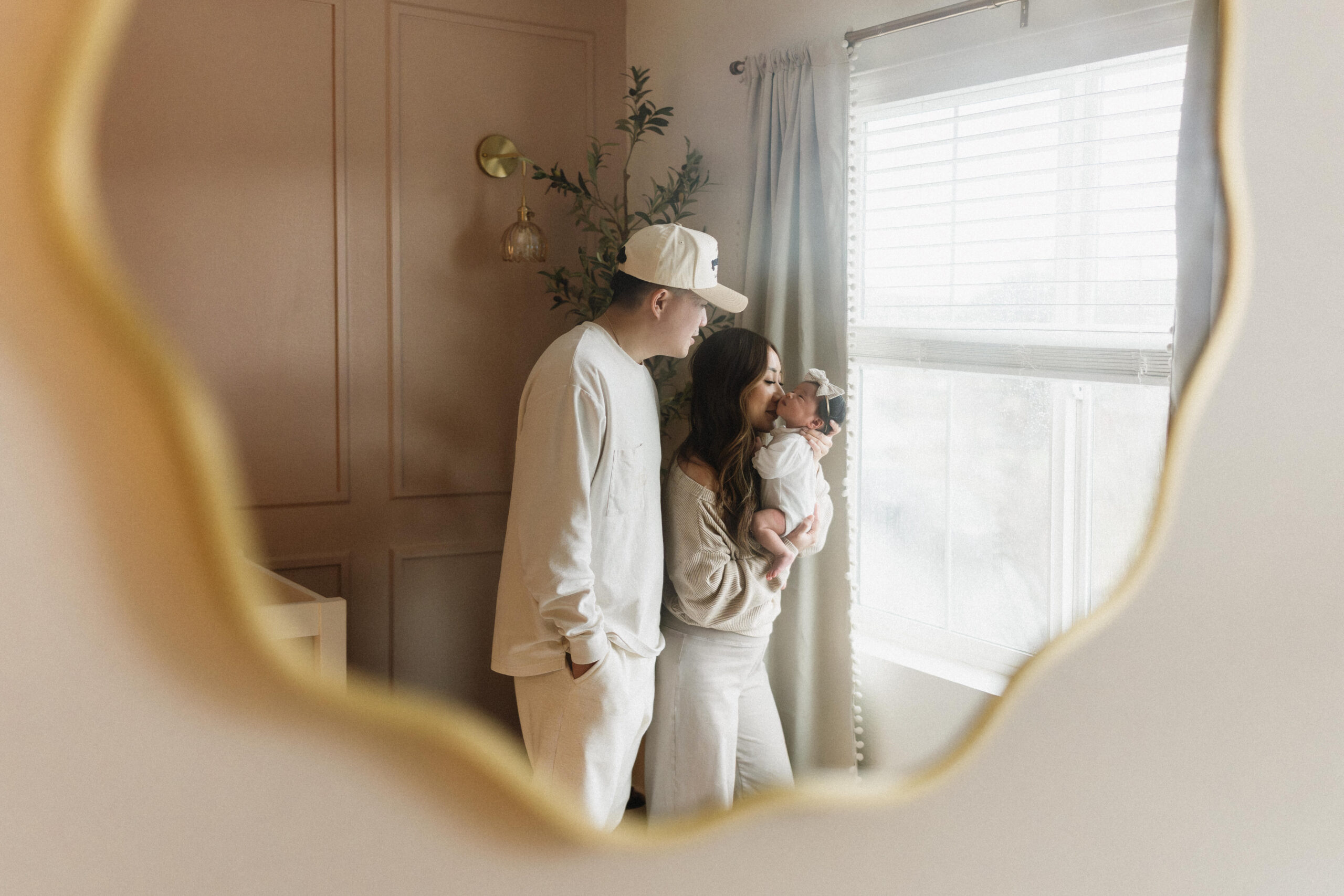 Mother gently holding her sleeping newborn during a calm in home newborn photoshoot by the window