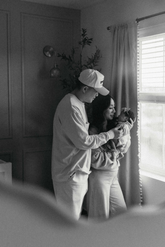 Mother gently holding her sleeping newborn during a calm in home newborn photoshoot by the window
