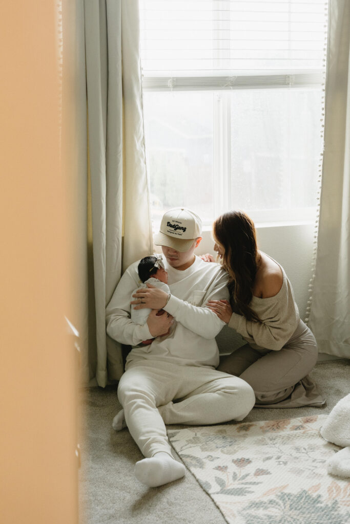 New parents cuddling their baby in a softly lit bedroom during a lifestyle family session
